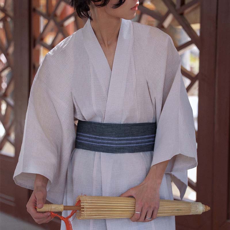 A Japanese man is wearing a samurai obi belt. The yukata is white. He is holding a Japanese bamboo parasol.