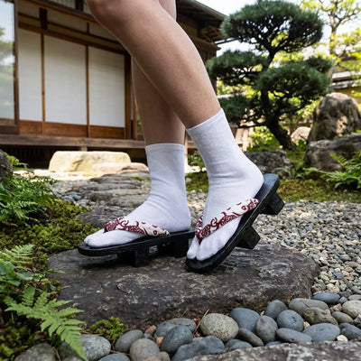 Sandal Japanese Woman in burgundy hanao and dark wood standing in a Japanese garden
