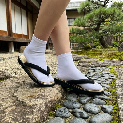 Sandals Japanese worn with white tabi socks, seen from a three-quarter angle in a Japanese garden