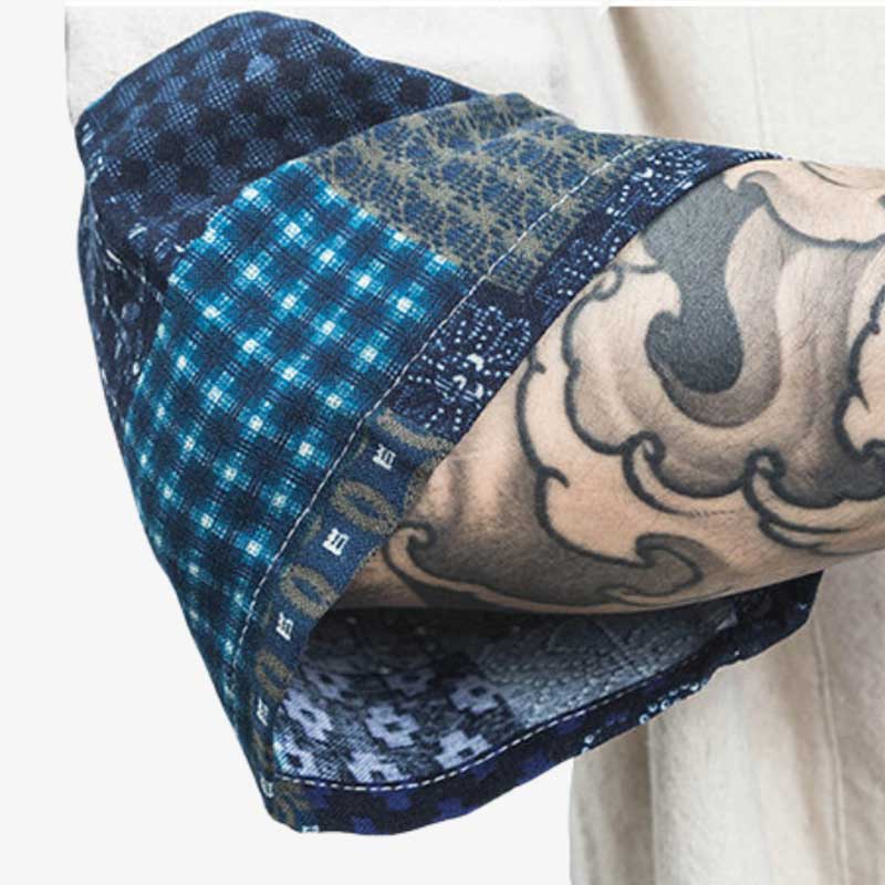 A man with a Japanese tattoo on his forearm is showing the sleeve of his short white cardigan kimono. The fabric of the sleeve is printed with geometric Japanese symbols
