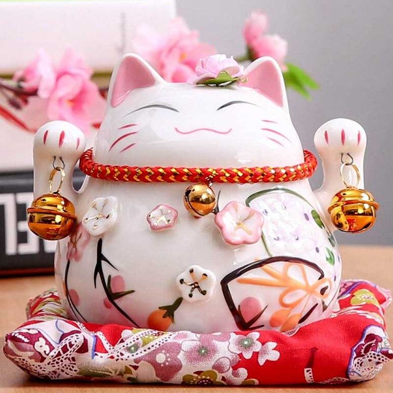 th statue maneki neko cat is a Japanese decorative object placed on a red cushion and a shelf.
