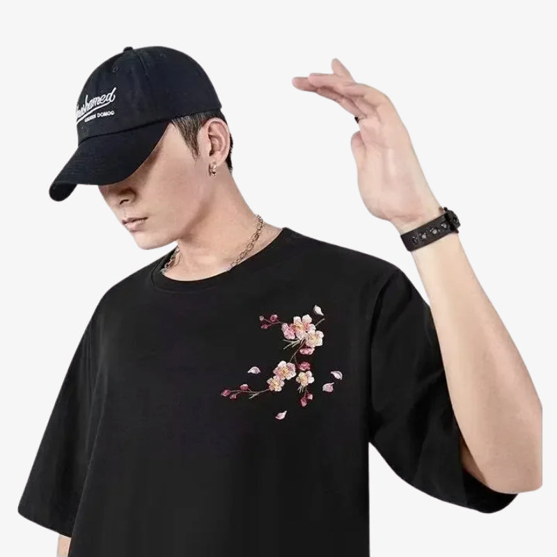 Person wearing a black t-shirt Sakura with floral design and a black cap on a white background