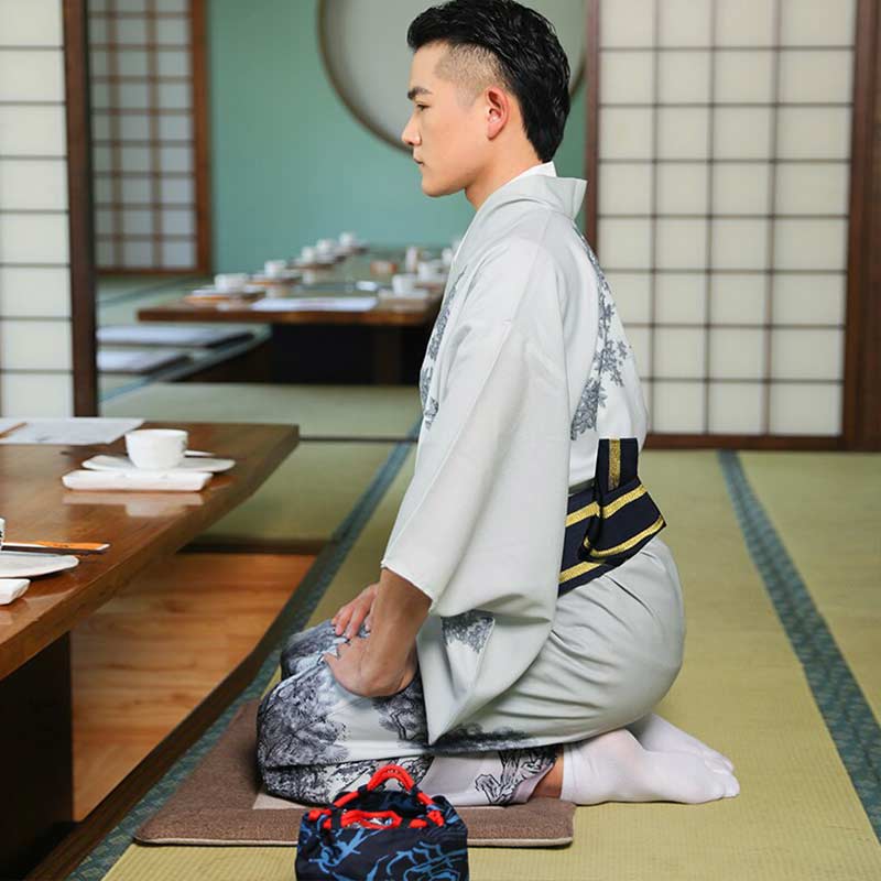 A man is sit on a tatami in a japanese tea house. He is dressed with a tea ceremony kimono men with a black and yellow obi belt in his back