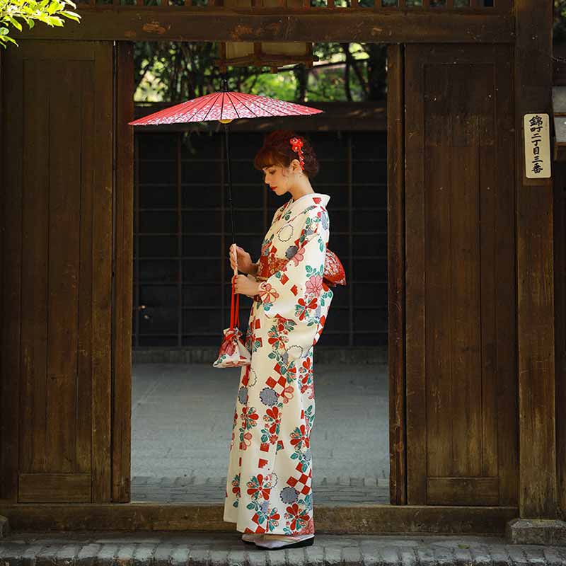 raditional elegant kimono dress in white with sakura and fukiwa flower designs. The woman holds a Japanese umbrella, enhancing the sophisticated look.