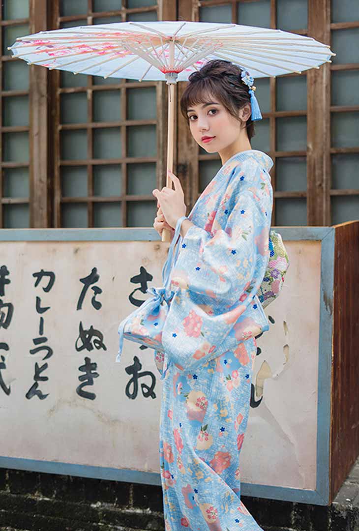 Traditional geisha dress kimono with printed Japanese floral designs. The woman elegantly holds a wagasa, showcasing the intricate patterns