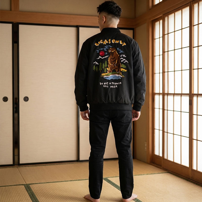 Person wearing a black traditional japanese bomber jacket with a bear graphic and text in a Japanese room with tatami mats and sliding Shoji doors.