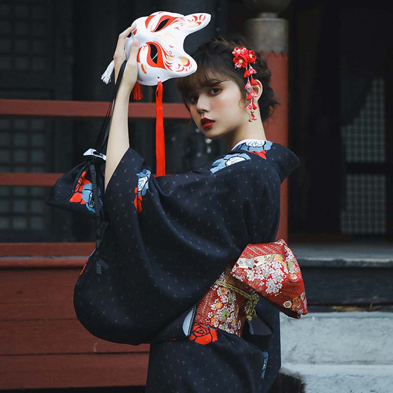 raditional kimono geisha featuring midnight blue fabric with red floral prints. The woman is standing, her kimono secured by a red Obi belt, her hair adorned with a red flower Kanzashi