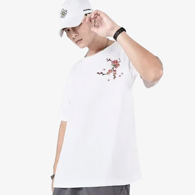 Person wearing a white Japanese sakura shirt with cherry blossom pattern embroidery and a white cap on a white background