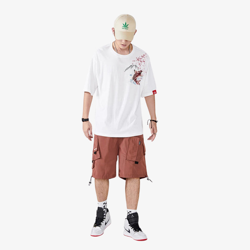 Person wearing a white Koi t-shirt with graphics, brown cargo shorts, and a beige cap on a white background