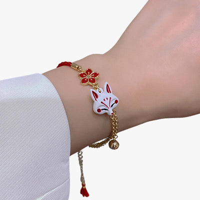 A woman wears a Japanese Kitsune bracelet with a gold chain, a Kitsune fox head and a sakura flower symbol on her wrist.