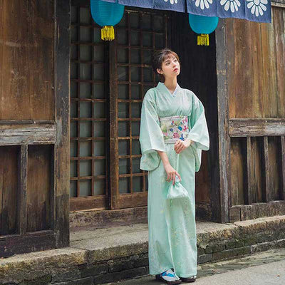Women Japanese dress kimono in white, featuring a subtle nature-inspired branch design on kimono materal. The woman stands with her kimono secured by an Obi belt