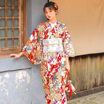 Women Japanese red kimono robe adorned with sakura flower motifs. The woman stands . She is dressed with a large obi Japanese belt