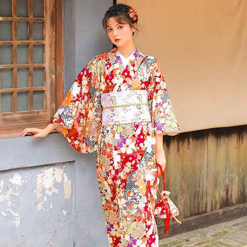 Women Japanese red kimono robe adorned with sakura flower motifs. The woman stands . She is dressed with a large obi Japanese belt