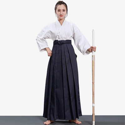 A Japanese martial artist dressed with womens hakama women, a white keikogi and holding a wooden shinai katana sword.