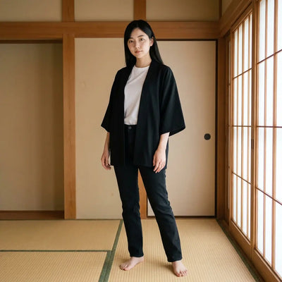 A womens kimono jacket in plain black, worn open over a white t-shirt and dark trousers in a tatami room with shoji screens.