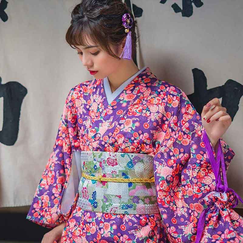 Yukata muji style with printed flower designs. A woman stands wearing this traditional Japanese kimono. The japanese outfit is closed with a japanese obi belt. The japanese girl has a hair jewel named kanzasho flower
