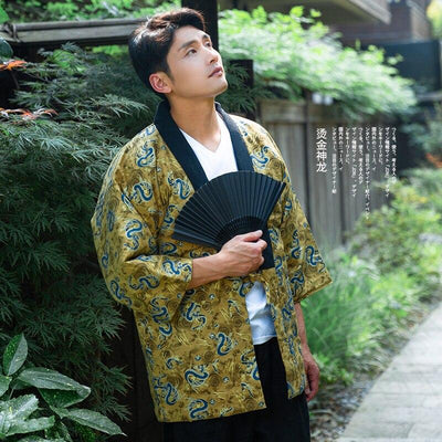 A person wearing a traditional Japanese hanten dragpm coat with golden yellow background and blue dragon motifs, holding a black fan.