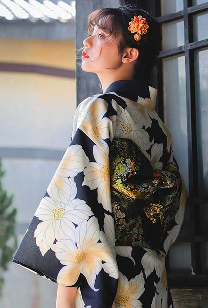uthentic Japanese kimono robe with yellow Japanese floral patterns. The woman wears a traditional flower kanzashi in her hair, completing the look.