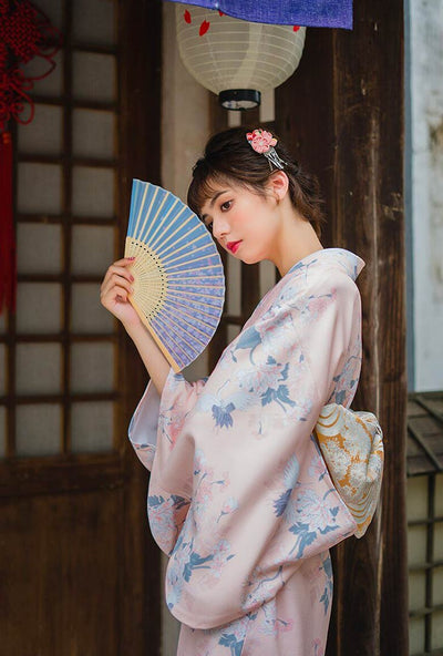 Charming Japanese kimono party costume cosplay fancy dress one size, featuring delicate flower prints on light fabric. The woman holds a sensu fan, her kimono fastened by a wide Obi belt