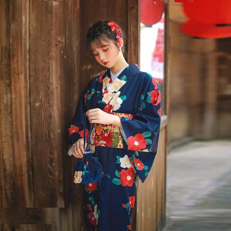 Japanese kimono robe yukata for women with traditional Japanese flower symbols printed on the fabric. The woman stands with her long kimono closed by an Obi bel