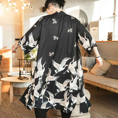 A man wearing a black kimono yukata haori jacket with white cranes and cherry blossom patterns.